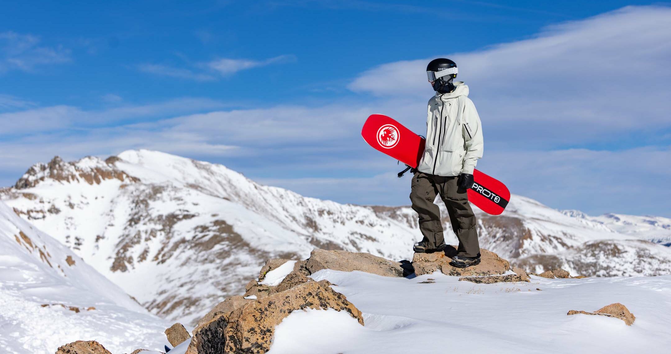 Snowboarder stands on top of ridgeline looking into the distance.