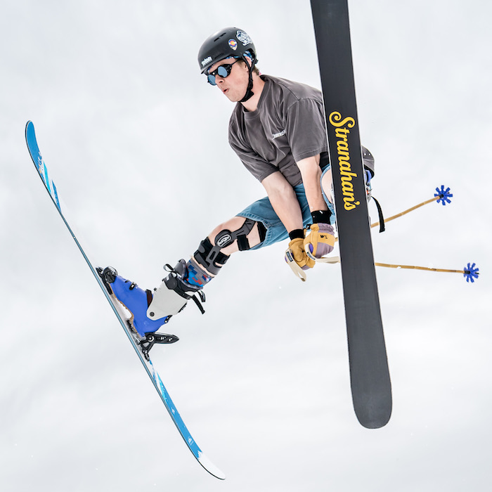 Airborn skier with skis outstretched and poles between his legs.