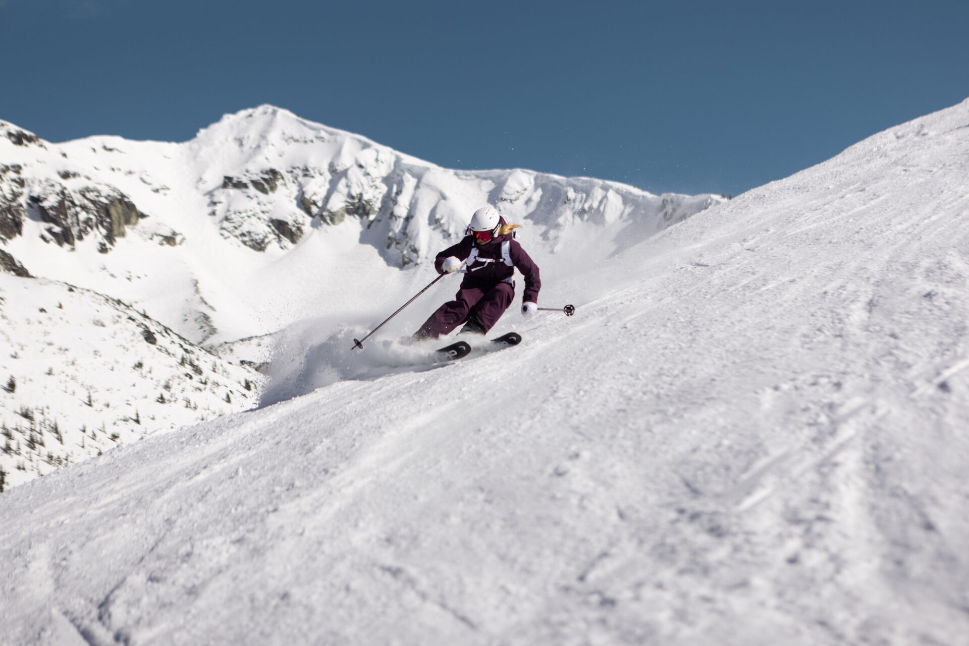 Skier carves a turn in front of a rocky, snowy mountain slope in the background.